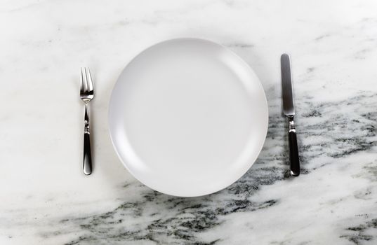 Dinner setting with clean plate, knife and fork on marble table  