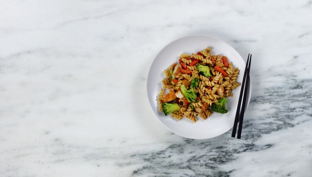 Dinner plate filled with healthy vegetables and noodles plus chopsticks as eating utensils 