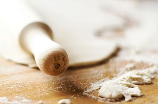 Wooden rolling pin on a wooden surface with some flour and a dough. Preparation of baked food