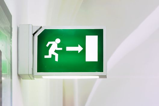 Illuminated green emergency exit sign. Stylized human figure running towards a door. Security and infographics