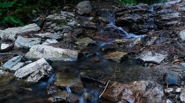 Close up mountain river flows between picturesque summer stones. Rocks in the mountains with water flowing