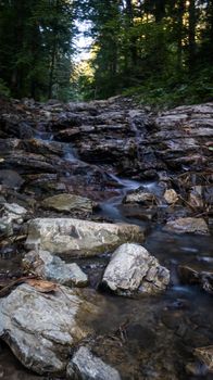 Close up mountain river flows between picturesque summer stones. Rocks in the mountains with water flowing