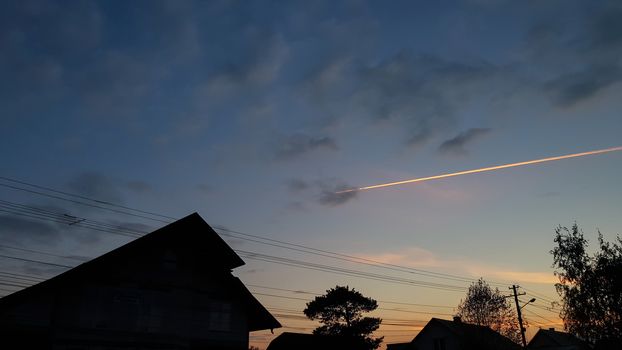 Orange sunset with clear sky and silhouette backlit houses and trees. Orange line of plane