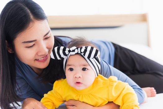 Portrait of beautiful young Asian mother playing and smiling together with his newborn little baby at home, Parent mom and little kid relaxing in the bedroom, Family having fun together