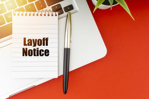LAYOFF NOTICE text with notepad, laptop, fountain pen and decorative plant on red background. Business and Copy Space Concept