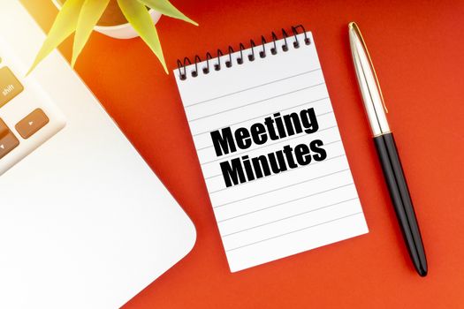 MEETING MINUTES text with notepad, laptop, fountain pen and decorative plant on red background. Business and Copy Space Concept