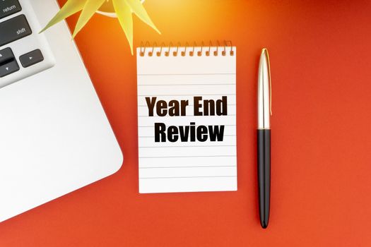 YEAR END REVIEW text with notepad, laptop, fountain pen and decorative plant on red background. Business and Copy Space Concept