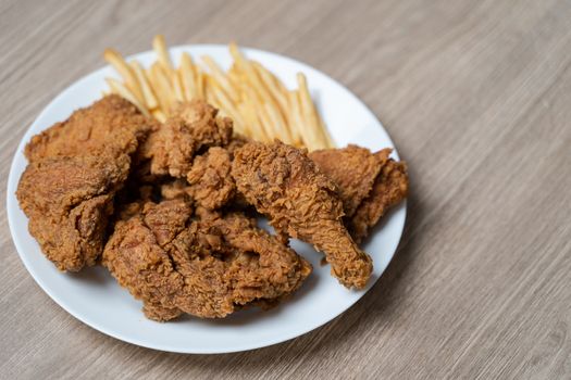 Crispy fried chicken with french fries in white plate on a wooden table.