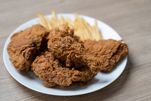 Crispy fried chicken with french fries in white plate on a wooden table.