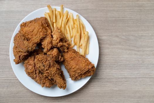 Crispy fried chicken with french fries in white plate on a wooden table.