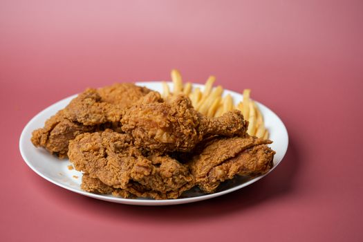 Crispy fried chicken with french fries in white plate on red background.