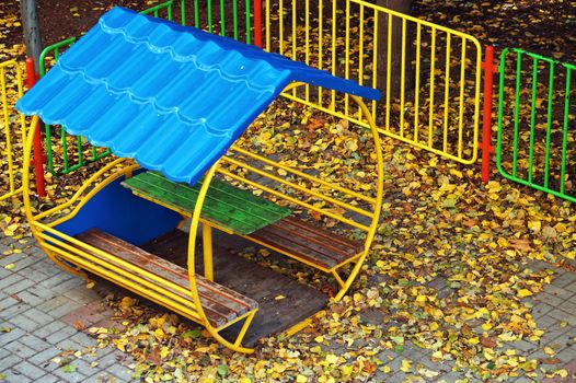 gazebo on the playground covered with yellow autumn leaves.