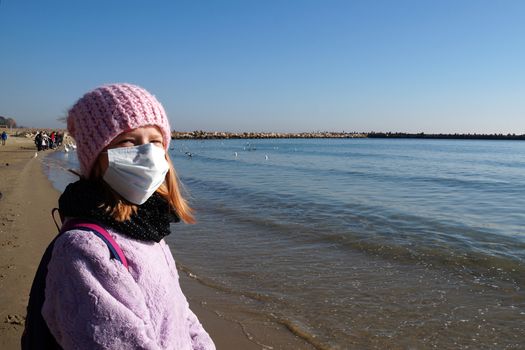 portrait of a teenage girl in a medical mask in an autumn on the sea.