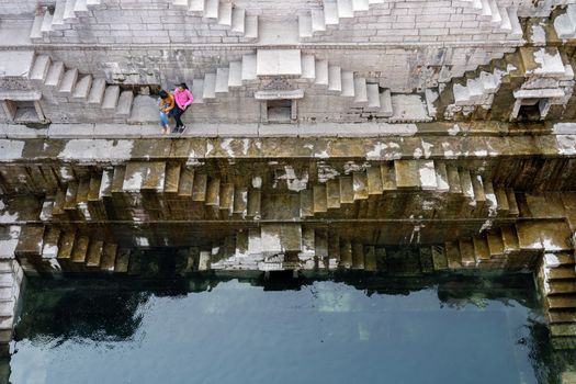 Jodhpur, India - December 8, 2019: Two girls sitting on the steps of the stepwell Toorji Ka Jhalra in the historic city centre.