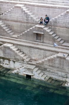 Jodhpur, India - December 8, 2019: A mother and her daughter sitting on the steps of the stepwell Toorji Ka Jhalra in the historic city centre.