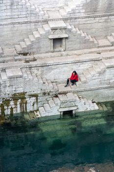 Jodhpur, India - December 8, 2019: A girl sitting on the steps of the stepwell Toorji Ka Jhalra in the historic city centre.