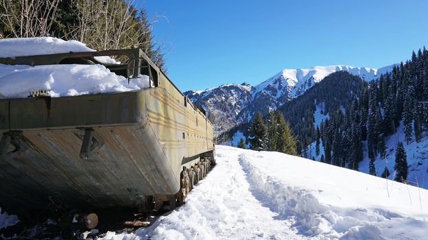 Abandoned military vehicles in the snowy mountains. Retro off-road machine military years. Machine in the mountains and forest. Blue sky and shadows. Abandoned tank on top of a hill.