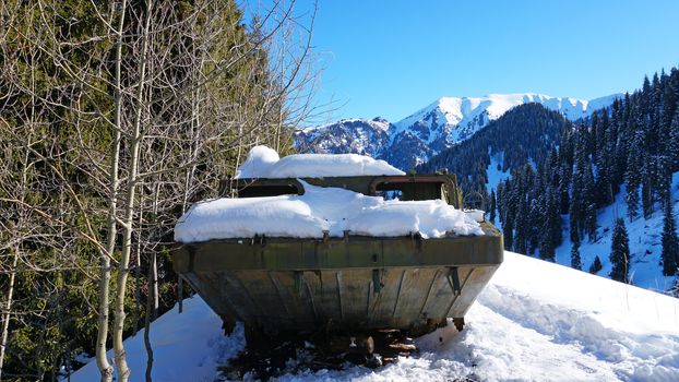 Abandoned military vehicles in the snowy mountains. Retro off-road machine military years. Machine in the mountains and forest. Blue sky and shadows. Abandoned tank on top of a hill.