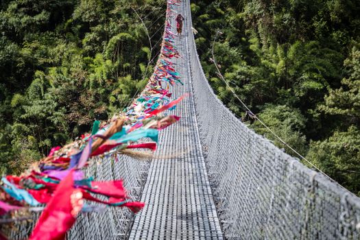 Ghasa, Nepal - November 05, 2014: Nepalese woman crossing a suspension bridge on the Annapurna Circuit.