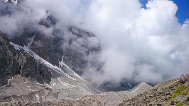 Glacier covered with rocks. Great cloud. Mountainous terrain, lots of big rocks, high mountains and snowy peaks. Huge ice covered the gorge. Small house is visible. Ratsek hut at an altitude of 3200m.