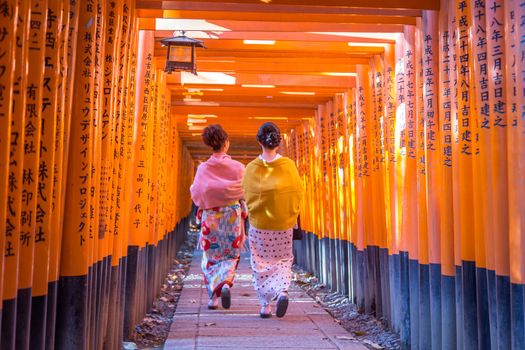 Kyoto, Japan - December 13, 2014: Two geishas walking through orange gates called torii at the Fushimi Inari Shrine
