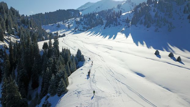 View from the height of the snowy mountains and forest. Huge clouds cover the hill in the distance. People are visible in places. Someone is running, resting, having a picnic or climbing to the top.