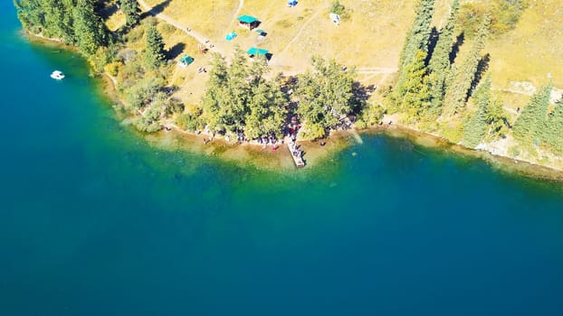 Kolsay lake among green hills and mountains. The mountain lake is surrounded by green forest, tall coniferous trees, grass and bushes. Clean water is like a mirror. Tourists swim on boats. Kazakhstan