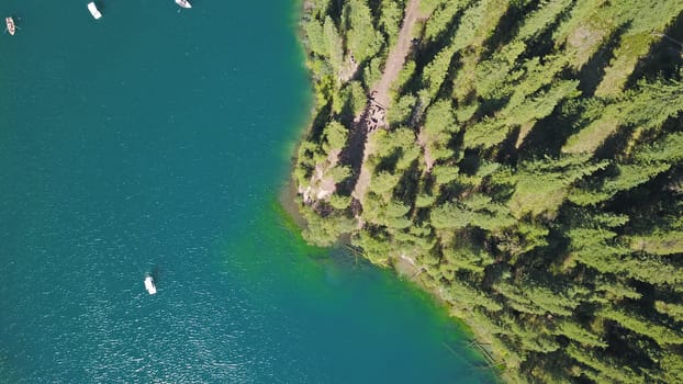 Kolsay lake among green hills and mountains. The mountain lake is surrounded by green forest, tall coniferous trees, grass and bushes. Clean water is like a mirror. Tourists swim on boats. Kazakhstan