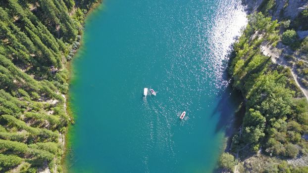 Kolsay lake among green hills and mountains. The mountain lake is surrounded by green forest, tall coniferous trees, grass and bushes. Clean water is like a mirror. Tourists swim on boats. Kazakhstan