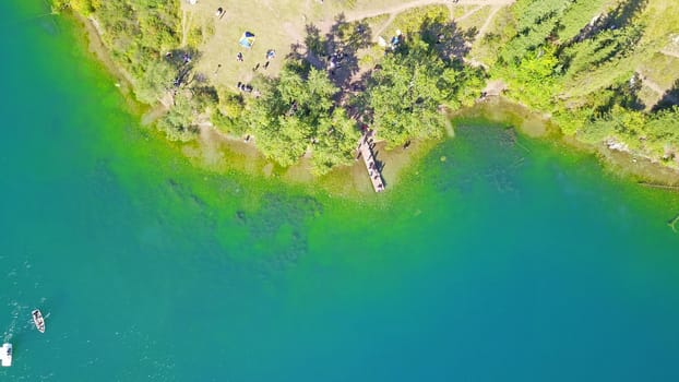 Kolsay lake among green hills and mountains. The mountain lake is surrounded by green forest, tall coniferous trees, grass and bushes. Clean water is like a mirror. Tourists swim on boats. Kazakhstan