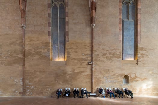 Toulouse, France - February 20, 2016: People sitting in chairs and listening to sounds in the huge hall in the Augustian convent.