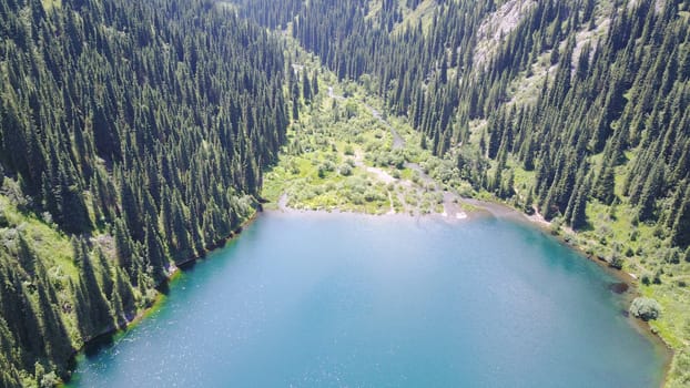 Kolsay lake among green hills and mountains. The mountain lake is surrounded by green forest, tall coniferous trees, grass and bushes. Clean water is like a mirror. Tourists swim on boats. Kazakhstan