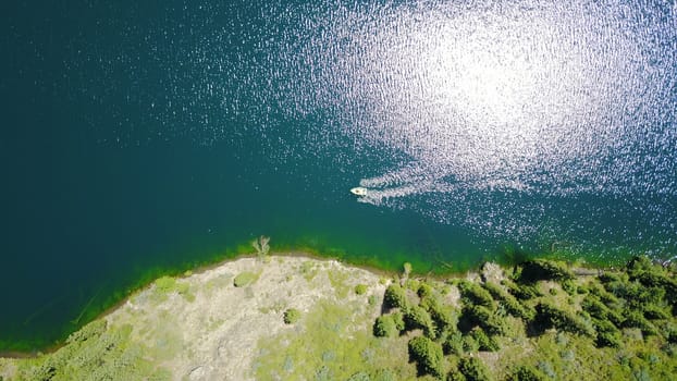 Kolsay lake among green hills and mountains. The mountain lake is surrounded by green forest, tall coniferous trees, grass and bushes. Clean water is like a mirror. Tourists swim on boats. Kazakhstan