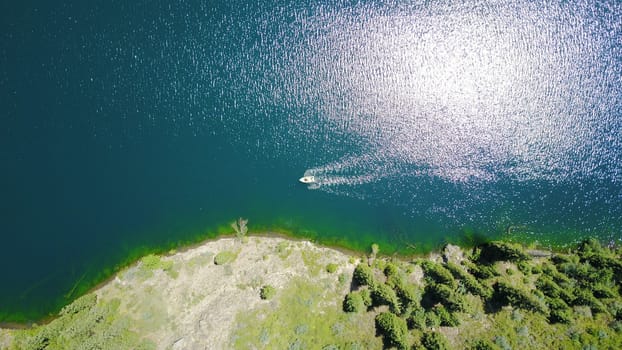 Kolsay lake among green hills and mountains. The mountain lake is surrounded by green forest, tall coniferous trees, grass and bushes. Clean water is like a mirror. Tourists swim on boats. Kazakhstan