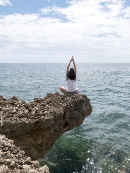 Rear view of young woman with long hair practicing yoga on rocks at sea