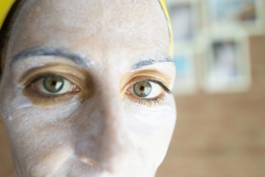 Relaxed woman applies mineral clay mask on face for rejuvenation, has headband on head