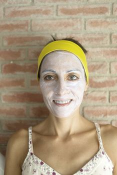 Relaxed woman applies mineral clay mask on face for rejuvenation, has headband on head