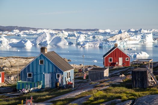 Rodebay, Greenland - July 09, 2018: Colorful wooden houses with icebergs in the background. Rodebay, also known as Oqaatsut is a fishing settlement north of Ilulissat.