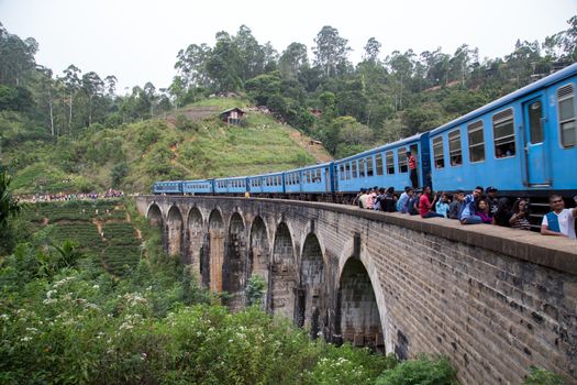 Demodara, Sri Lanka - August 5, 2018: People next to a blue train crossing the famous Nine Arch Bridge