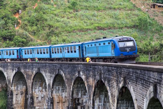 Demodara, Sri Lanka - August 5, 2018: People next to a blue train crossing the famous Nine Arch Bridge