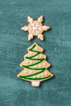 Top view of Christmas tree and snowflake cooikes with gingerbread man wearing mask on green table background.