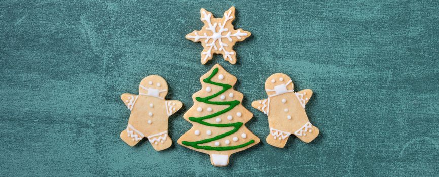 Top view of Christmas tree and snowflake cooikes with gingerbread man wearing mask on green table background.