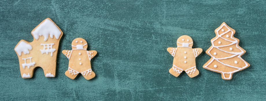 Top view of Christmas tree and snowflake cooikes with gingerbread man wearing mask on green table background.