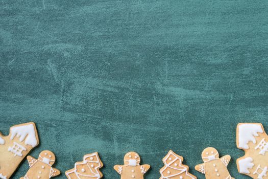 Top view of Christmas tree and snowflake cooikes with gingerbread man wearing mask on green table background.