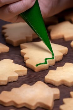 Close up of drawing gingerbread Christmas tree sugar cookie on wooden table background with green icing, concept of holiday celebration.