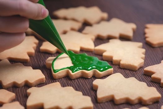 Close up of drawing gingerbread Christmas tree sugar cookie on wooden table background with green icing, concept of holiday celebration.