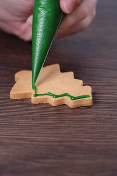 Close up of drawing gingerbread Christmas tree sugar cookie on wooden table background with green icing, concept of holiday celebration.