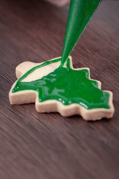 Close up of drawing gingerbread Christmas tree sugar cookie on wooden table background with green icing, concept of holiday celebration.
