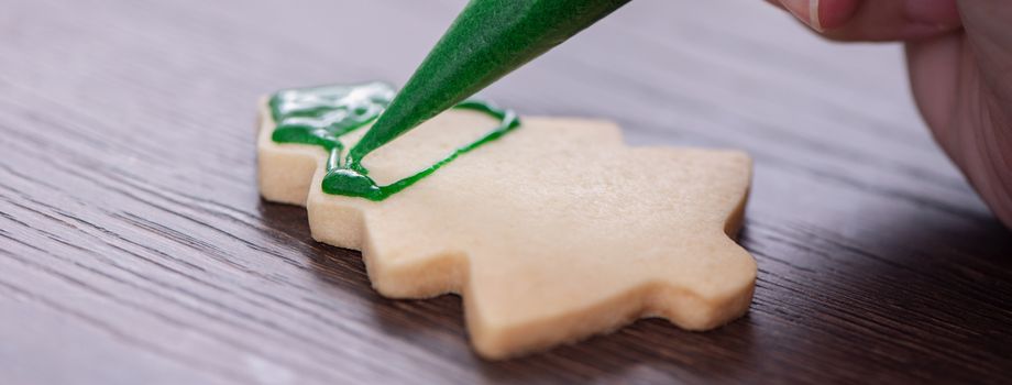 Close up of drawing gingerbread Christmas tree sugar cookie on wooden table background with green icing, concept of holiday celebration.