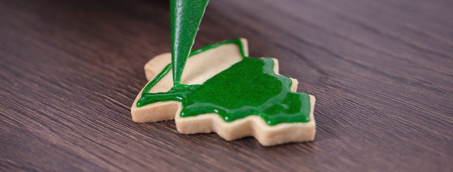 Close up of drawing gingerbread Christmas tree sugar cookie on wooden table background with green icing, concept of holiday celebration.